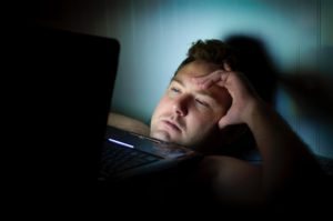 un homme regarde un écran dans le noir : la lumière bleue l'ébloui et est néfaste pour bien dormir